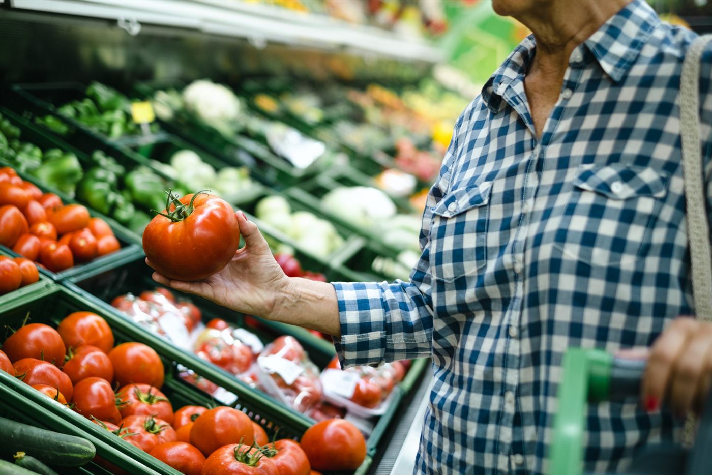 A shopper choosing a fresh tomato from a supermarket produce display