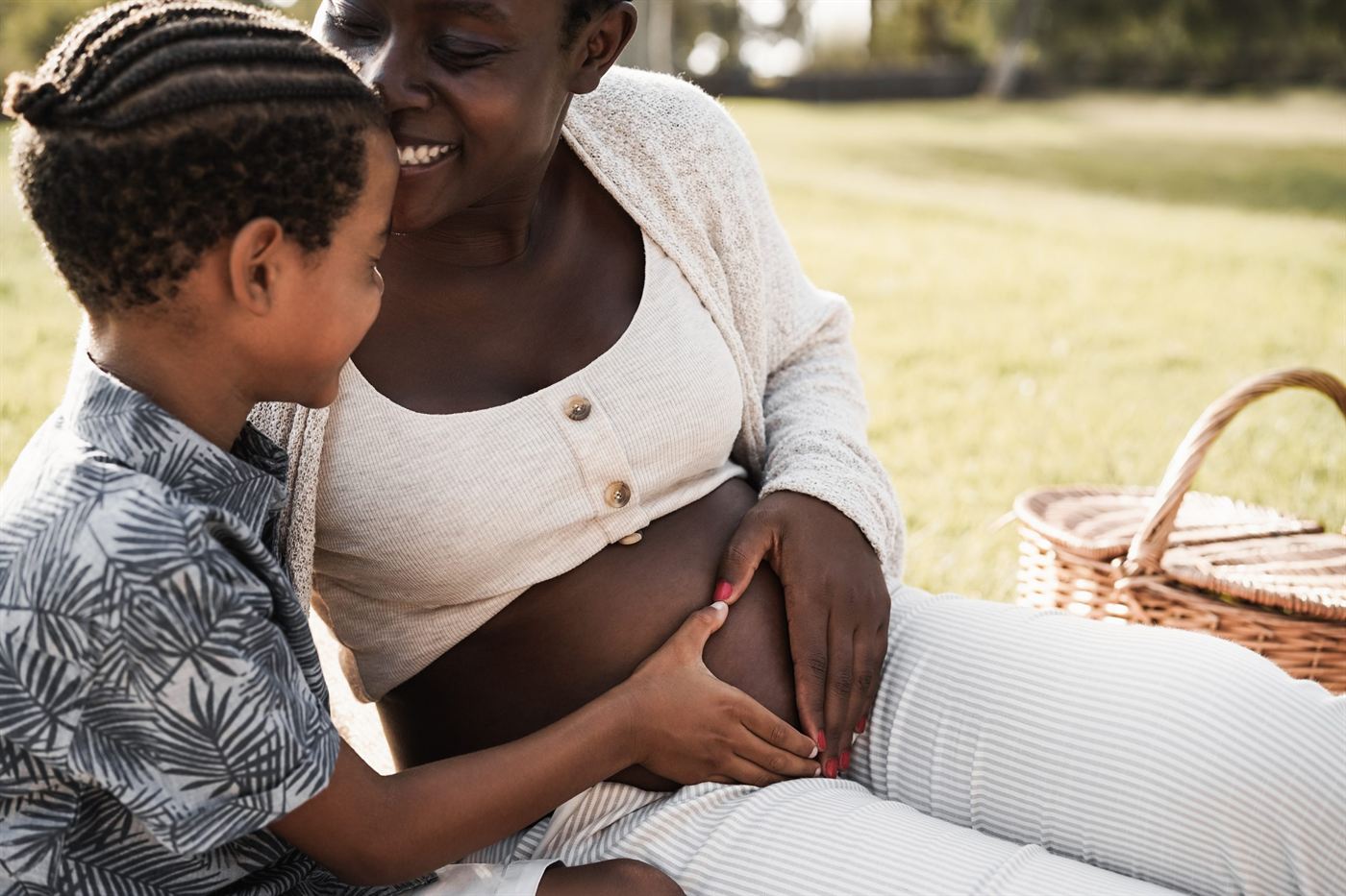 An expectant mother and her young son sitting together on a picnic blanket